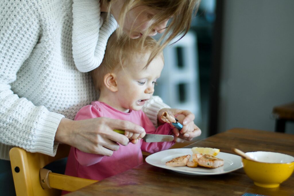 a mother teaching a baby how to eat using a knife and fork