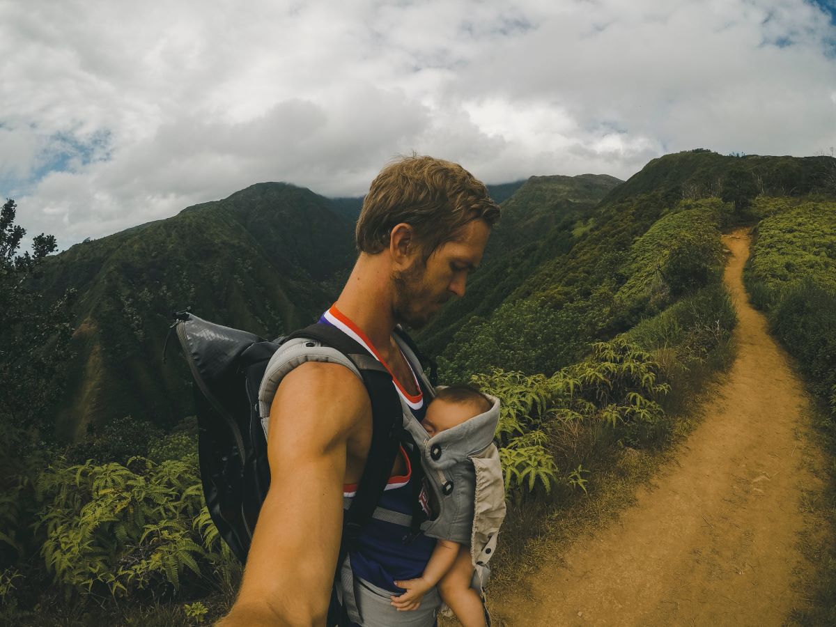 a man hiking carrying a baby in a grey soft structured carrier