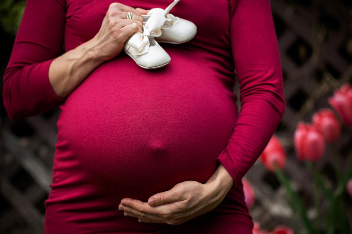 a pregnant woman holding baby shoes