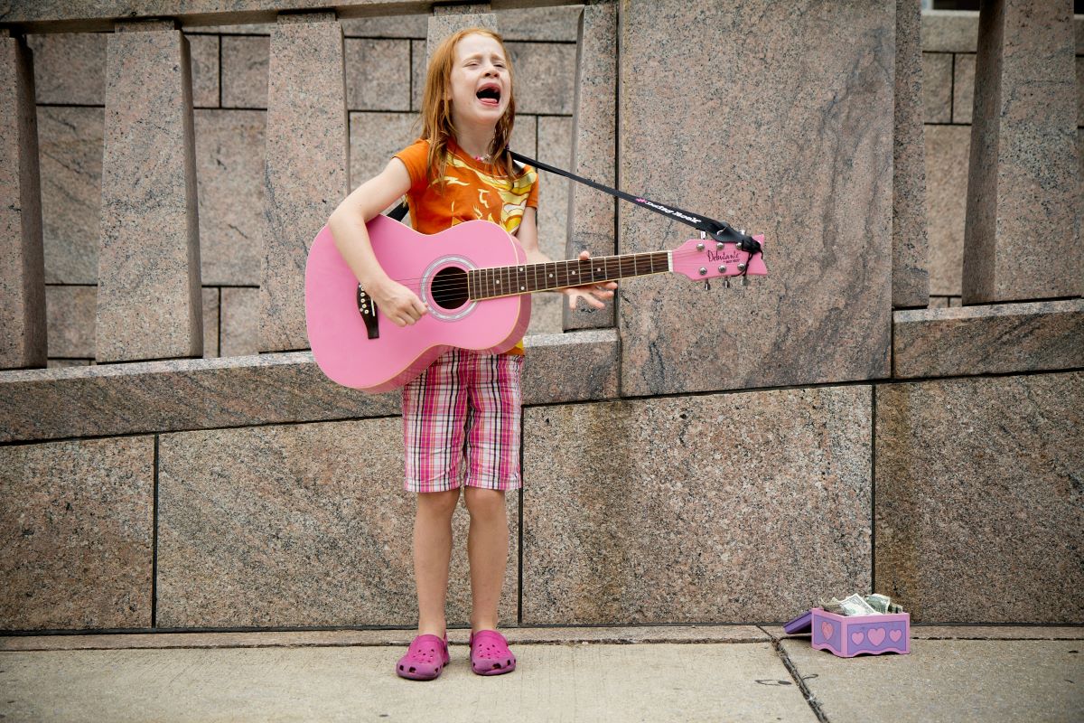 a girl singing and playing guitar near a wall