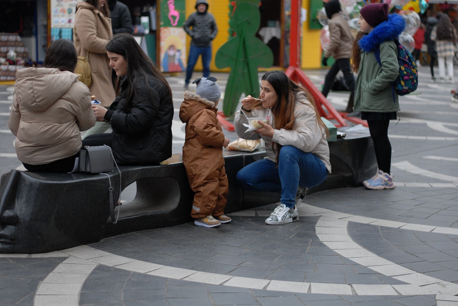 women and children eating sitting on a town square sit